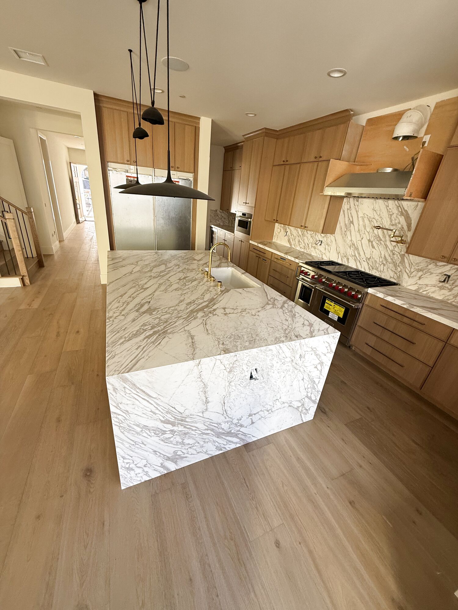 Marble waterfall island with a bookmatched slab and a gold faucet, set by Gallegos Custom Tile.
