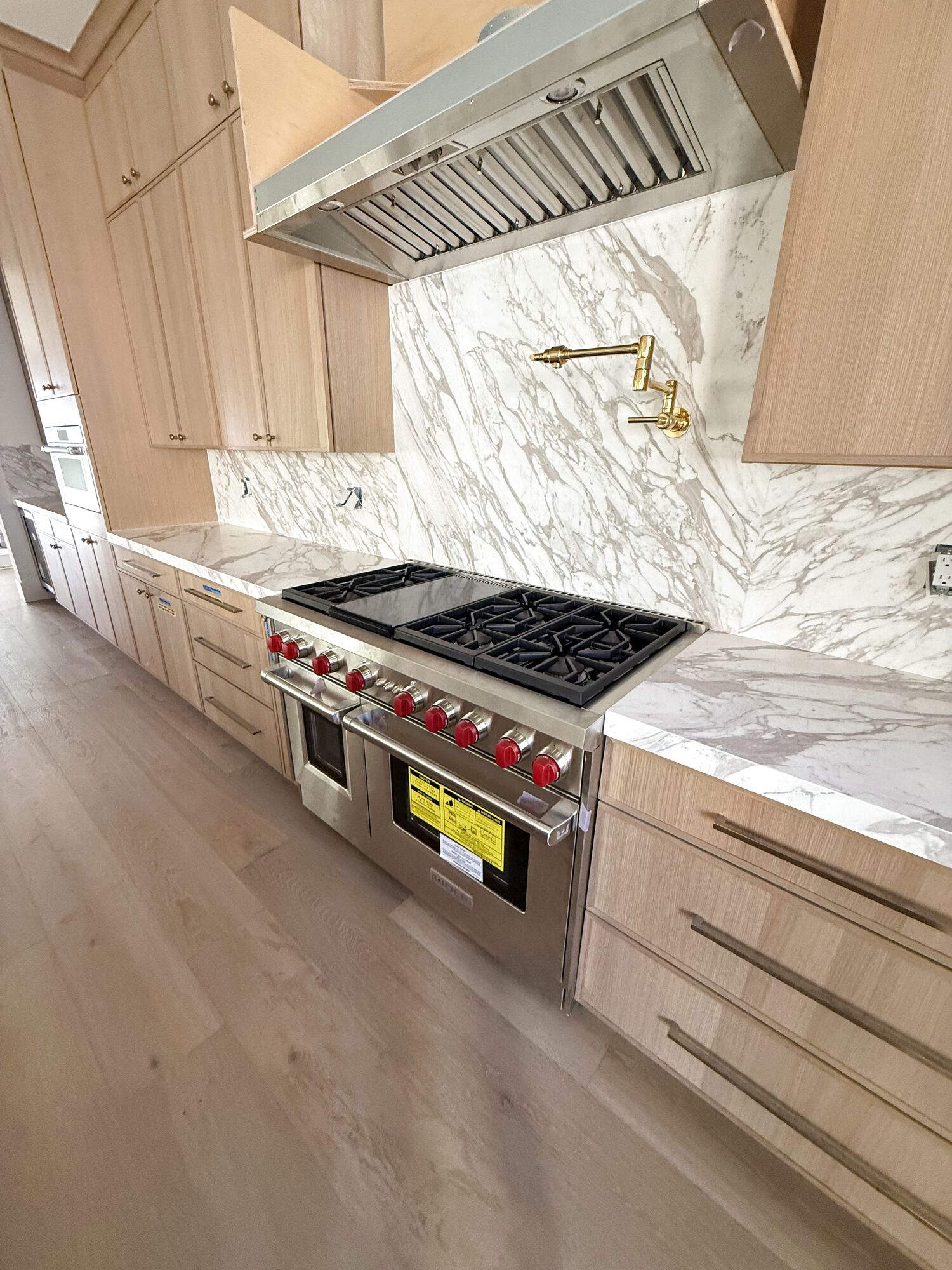 Full-height marble backsplash behind a range, with a brass pot filler, set by Gallegos Custom Tile.