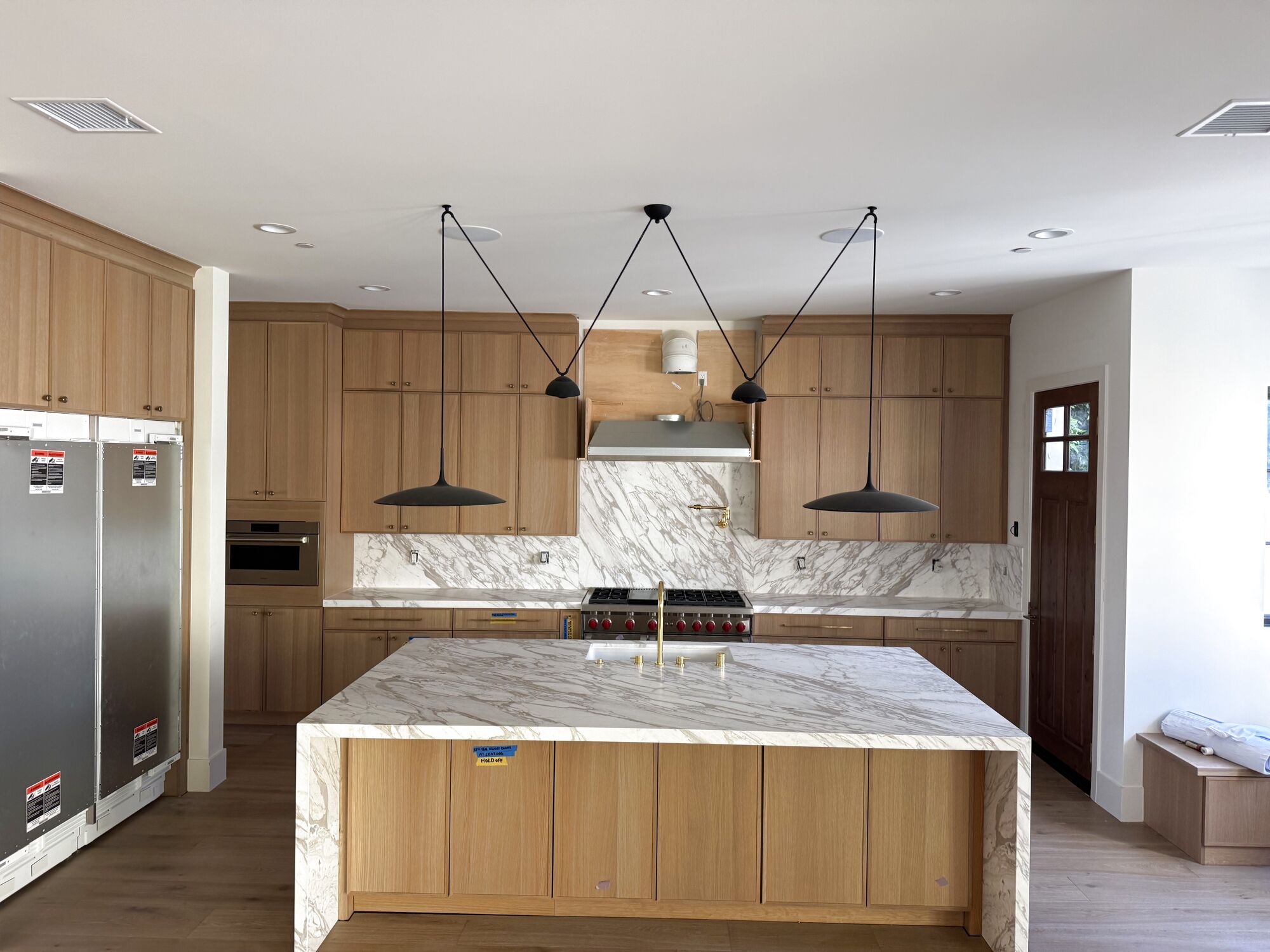 Gallegos Custom Tile: a light oak kitchen with a marble waterfall island, full-height marble backsplash, and slab counters. The house is still being finished around the stone.